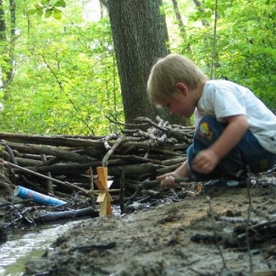 Criança brincando junto a riacho em floresta com torre de madeira