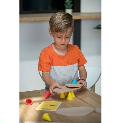 Menino brinca com jogo de cones coloridos e base de madeira numa mesa