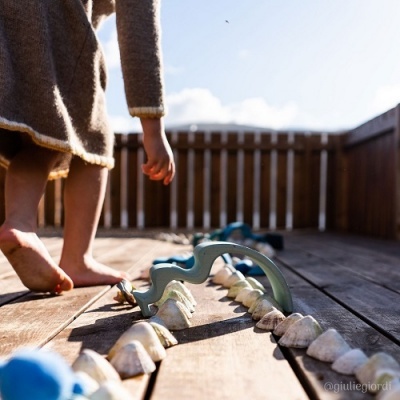 Criança descalça com brinquedo de plástico azul e dentes brancos numa varanda de madeira
