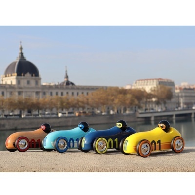 Carros de brinquedo retro em madeira de várias cores com número 01 numa superfície exterior com rio e edifícios ao fundo