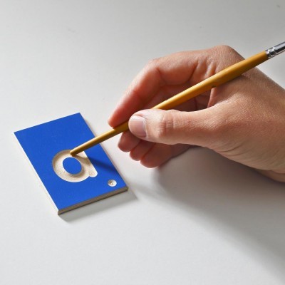 Mão a pintar a letra 'a' gravada num bloco azul com pincel