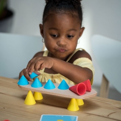 Criança brincando com brinquedo de equilíbrio colorido numa mesa de madeira