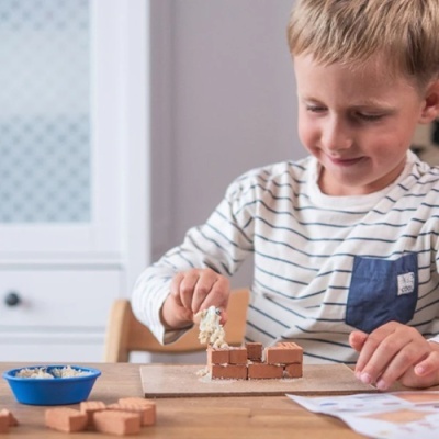 Criança a construir muro com tijolos de brinquedo e tabuleiro de madeira