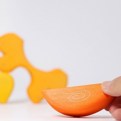 Brinquedo de madeira laranja com padrão espiral segurado por mão, peças de madeira ao fundo