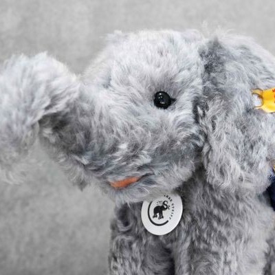 Elefante de peluche cinzento com etiqueta Steiff Classic na orelha e manta azul amarela
