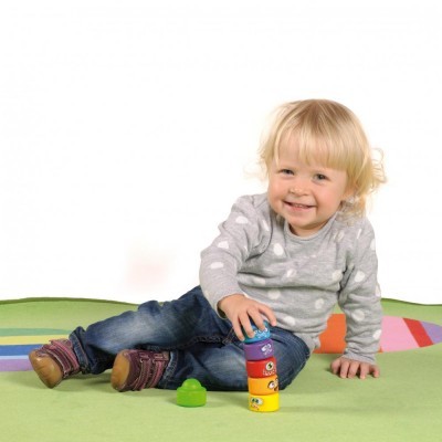 Bebé a brincar com brinquedo de empilhar colorido sentado num tapete verde