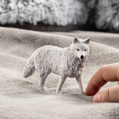 Figurine de lobo branco sobre tecido cinzento com uma mão ao lado para comparação de tamanho