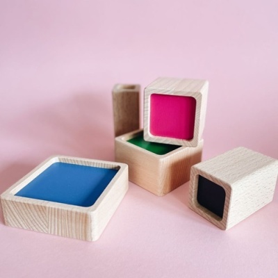 Blocos sensoriais de madeira com superfícies coloridas em fundo rosa.