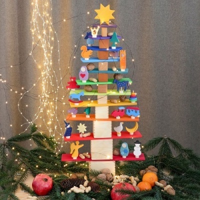 Árvore de Natal de madeira decorativa com animais coloridos e luzes, rodeada por frutas e pinheiro