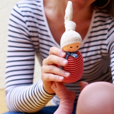 Boneco de tecido listrado vermelho e branco com cabeça de pano sendo segurado por pessoa com camisa listrada