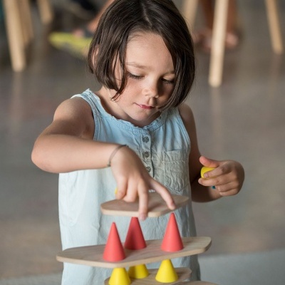 Menina a jogar com brinquedo de madeira com plataformas e cones coloridos.