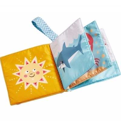 Livro infantil de tecido com páginas coloridas e ilustrações de sol, tubarão e padrão colorido