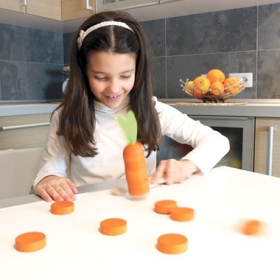Menina brincando com peças laranjas em forma de cenoura numa mesa branca de cozinha moderna