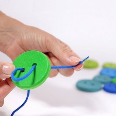 Botões de plástico coloridos com cordão azul em mãos, fundo branco