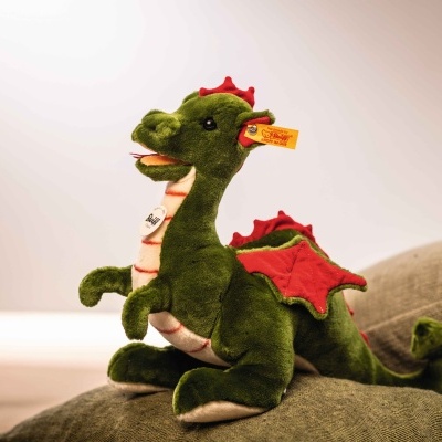 Pelúcia de dragão verde com asas vermelhas em almofadas cinzentas