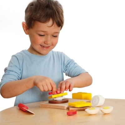 Criança a brincar com brinquedos de comida em madeira colorida numa mesa