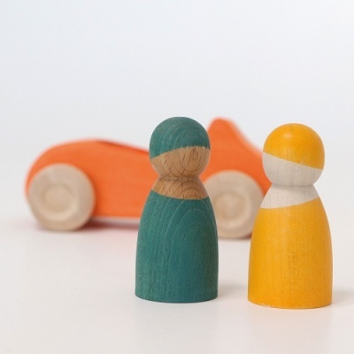 Figuras humanas em madeira verde e amarelo com carro laranja ao fundo.