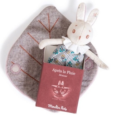 Boneco peluche coelho branco com roupa azul floral em caixa vermelha sobre almofada em forma de folha cinzenta