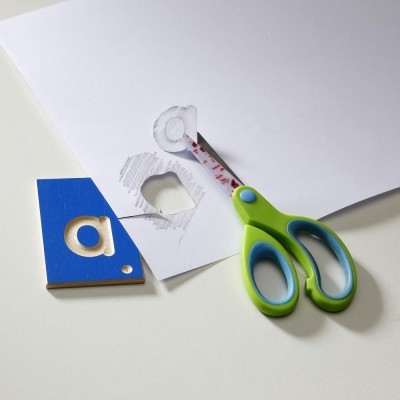 Tesouras verdes e cartão azul com letra 'a' recortada sobre fundo branco
