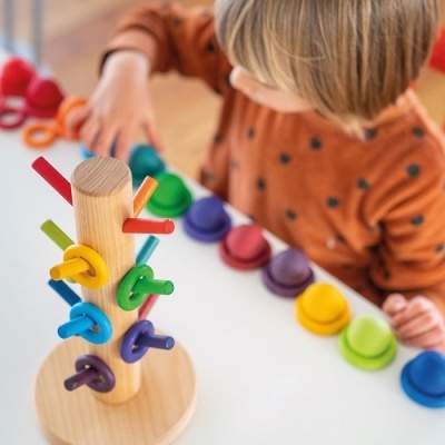 Brinquedo educativo de madeira com anéis coloridos e criança a brincar ao fundo
