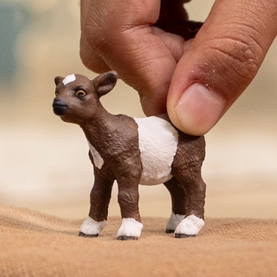 Miniatura de animal castanha e branca segurada por dedos