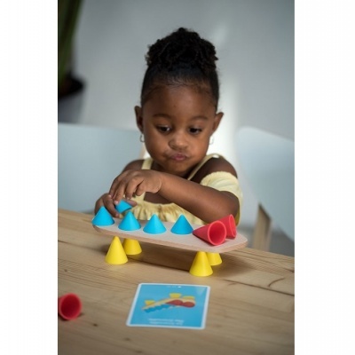 Criança a brincar com jogo de equilíbrio de cones coloridos numa mesa de madeira