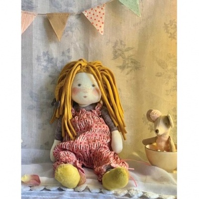 Boneca de pano com cabelo amarelo de lã e roupa rosa sentada ao lado de brinquedo de rato