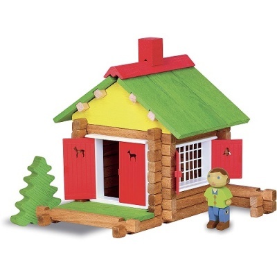 Casa de brincar em madeira com telhado verde e portas vermelhas ao lado da árvore de madeira e boneco.