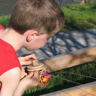 Criança com brinquedo de madeira e cesta colorida ao ar livre perto de guarda-corpo de madeira