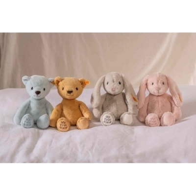 Quatro peluches coloridos sentados em cama branca com fundo bege
