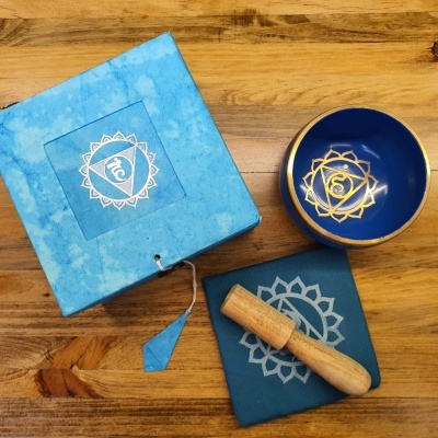 Conjunto de tigela sonora azul com símbolo dourado, caixa azul, pano azul e martelo de madeira sobre superfície de madeira