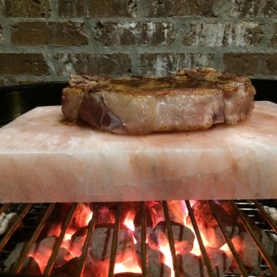 Bife a grelhar sobre placa de sal rosa com brasas em grelha