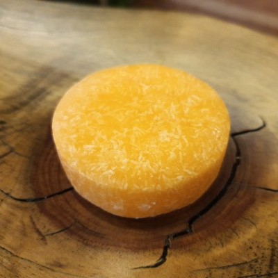 Sabonete sólido laranja claro com partículas brancas em madeira