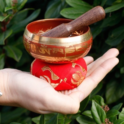 Tigela de som tibetana dourada com almofada vermelha em mão aberta