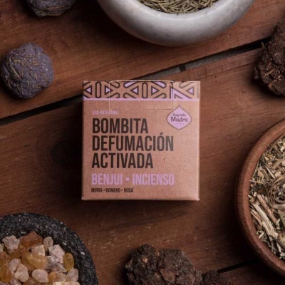 Caixa de Bombita Defumación Activada Benju + Incienso sobre mesa de madeira rodeada por tigelas com resinas e ervas.