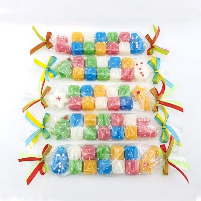 Cinco sacos transparentes com laços coloridos contendo cubos coloridos com letras brancas e pontos, sobre fundo branco.