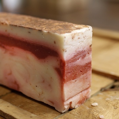 Barra de sabão artesanal com camadas creme e vermelho sobre madeira