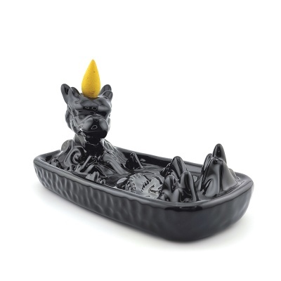 Incensário preto em forma de cachorro com chifre e incenso amarelo no topo, visto de lado