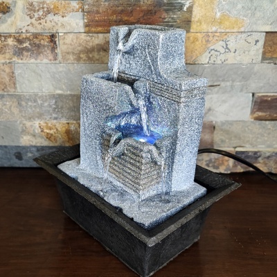 Fonte decorativa em pedra com água e luz azul sobre mesa de madeira