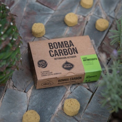 Embalagem de produto Bomba Carbón sobre chão de pedra rodeado por objetos amarelos redondos e plantas verdes