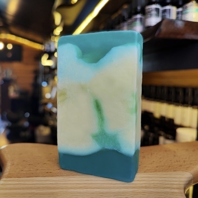 Sabonete artesanal azul, branco e verde sobre superfície de madeira em loja com prateleiras