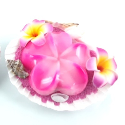 Vela rosa em forma de flor numa concha com decorações de areia e conchas