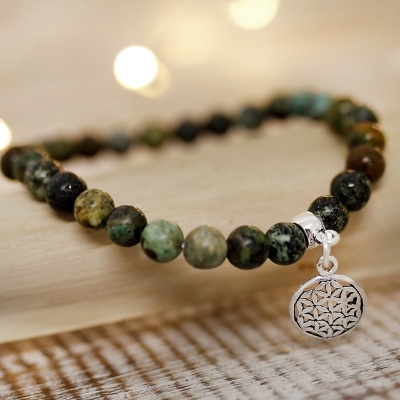 Pulseira de pedras naturais verdes com pendente prateado sobre madeira clara