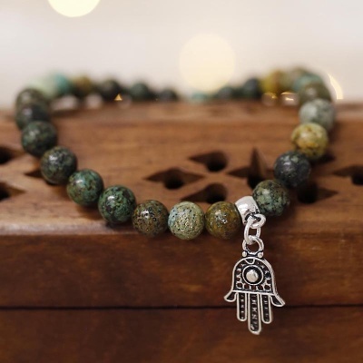 Pulseira de contas verdes e castanhas com pendente de mão prateada sobre madeira