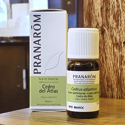 Óleo essencial Pranarôm Cedro del Atlas em frasco de vidro castanho com tampa branca e caixa branca verde sobre madeira