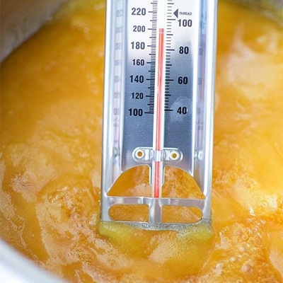 Termómetro culinário metálico em líquido dourado fervente numa panela