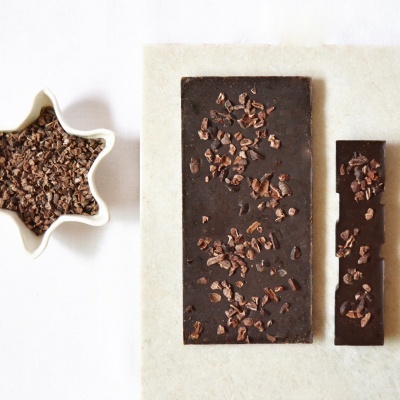 Duas barras de chocolate preto com pedaços de cacau ao lado de uma tigela branca em forma de estrela com pedaços de cacau