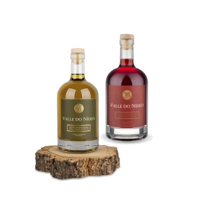 Duas garrafas de bebida Valle do Nídeo, uma verde-oliva e outra vermelha, com rótulos dourados, uma sobre pedaço de madeira rústica