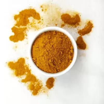 Pó amarelo-alaranjado num recipiente branco redondo com pó espalhado ao redor