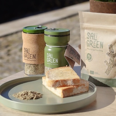 Produtos SALi GREEN incluindo tempero em vidro, moedor e pão numa bandeja verde ao ar livre